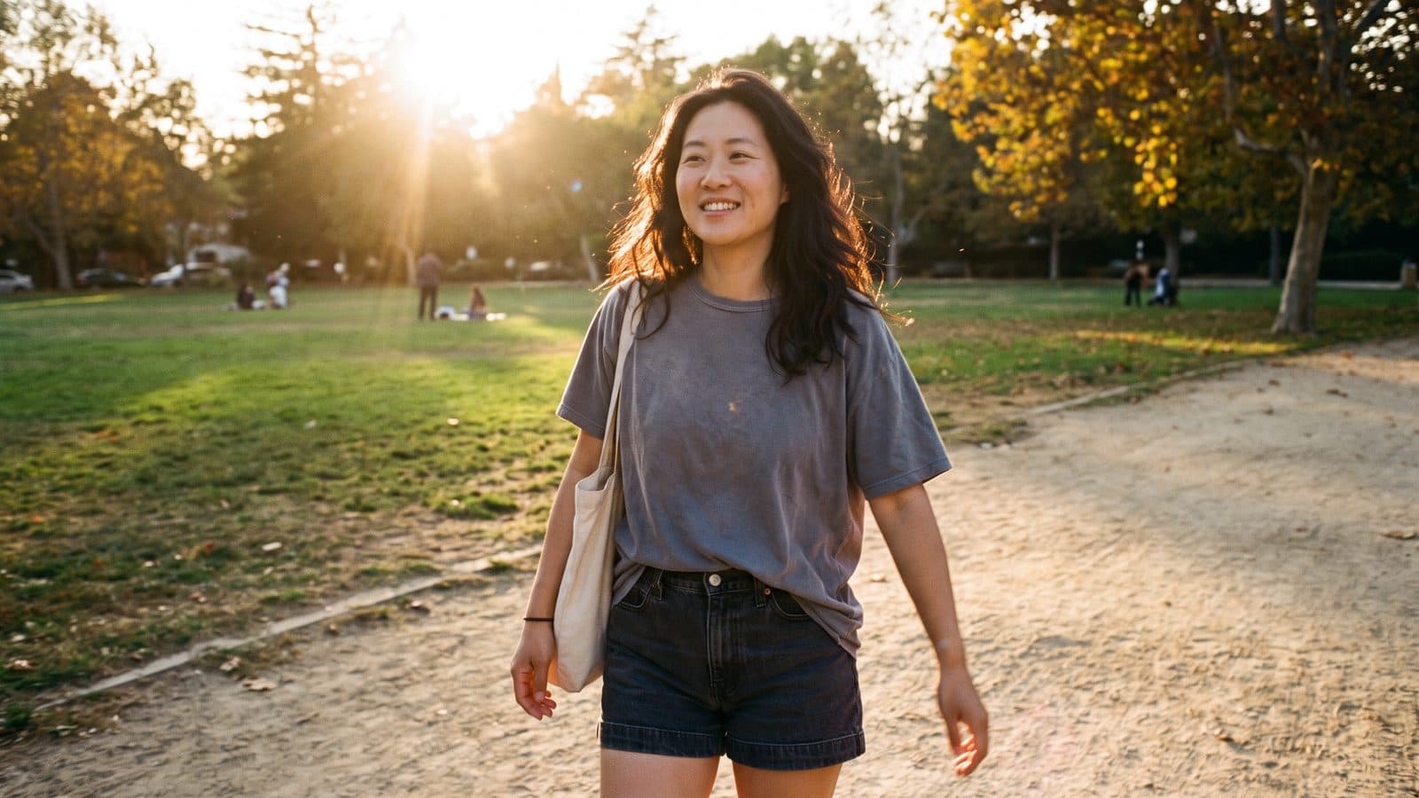 A woman walking along a park path in low evening sunlight.